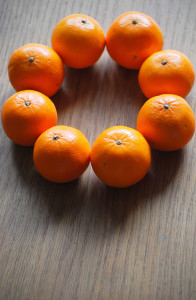 8 small oranges arranged in a circle on a wooden table top