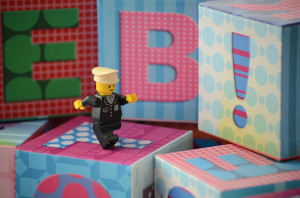 A small lego figure marching across some alphabet blocks towards the right