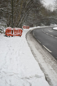 Red plastic barriers around lamposts in the snow by the side of a curving road