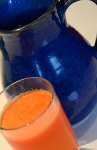Blue ceramic jug next to a small glass of bright orange carrot, apple & ginger juice