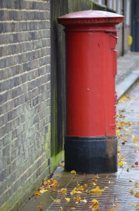 Red letterbox on a wet day with leaves on the foor