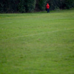 Long shot across a park towards a small figure in a red jacket with his back to the camera