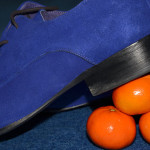 Bright blue suede shoe with its heel balanced on 3 satsumas