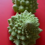 Two Romanesco cauliflower next to each other on a red background